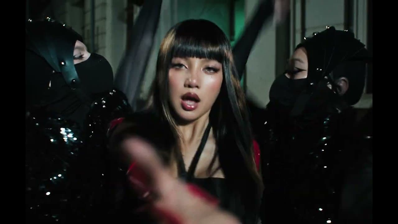 LISA, with long dark hair and a red-and-black outfit, raps toward the camera between two masked dancers in a night street scene of the 'SaWaDiKa' music video