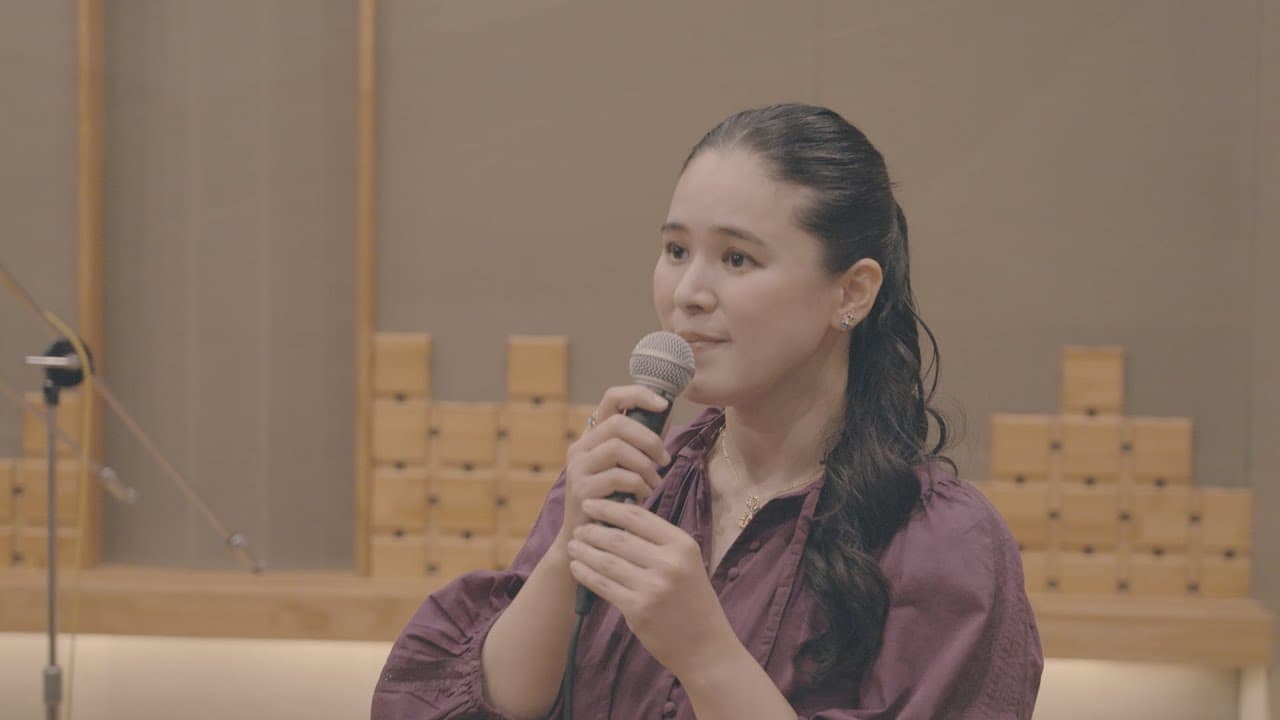 Aoi Teshima, in a plum-coloured blouse with her dark hair tied back, sings into a hand-held microphone in a recording studio lined with wooden acoustic blocks, in her 2025 studio performance of 'Mori no Chiisana Restaurant'