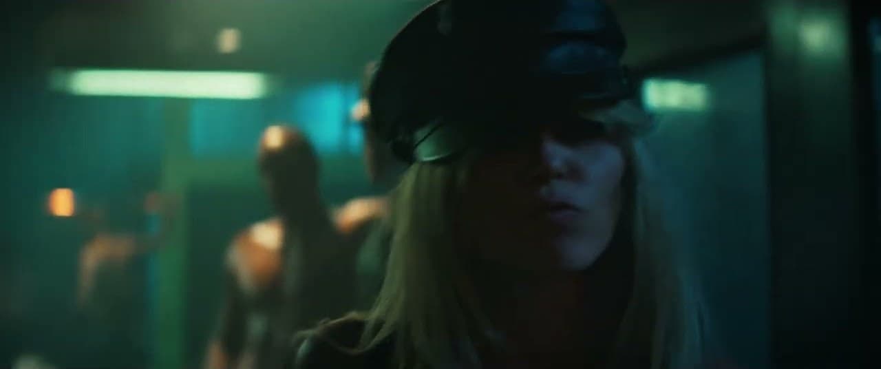 Miley Cyrus 'Bass Persuades' MV capture: Miley Cyrus in a black leather peaked cap, her face half in shadow, with dancers behind her in green light