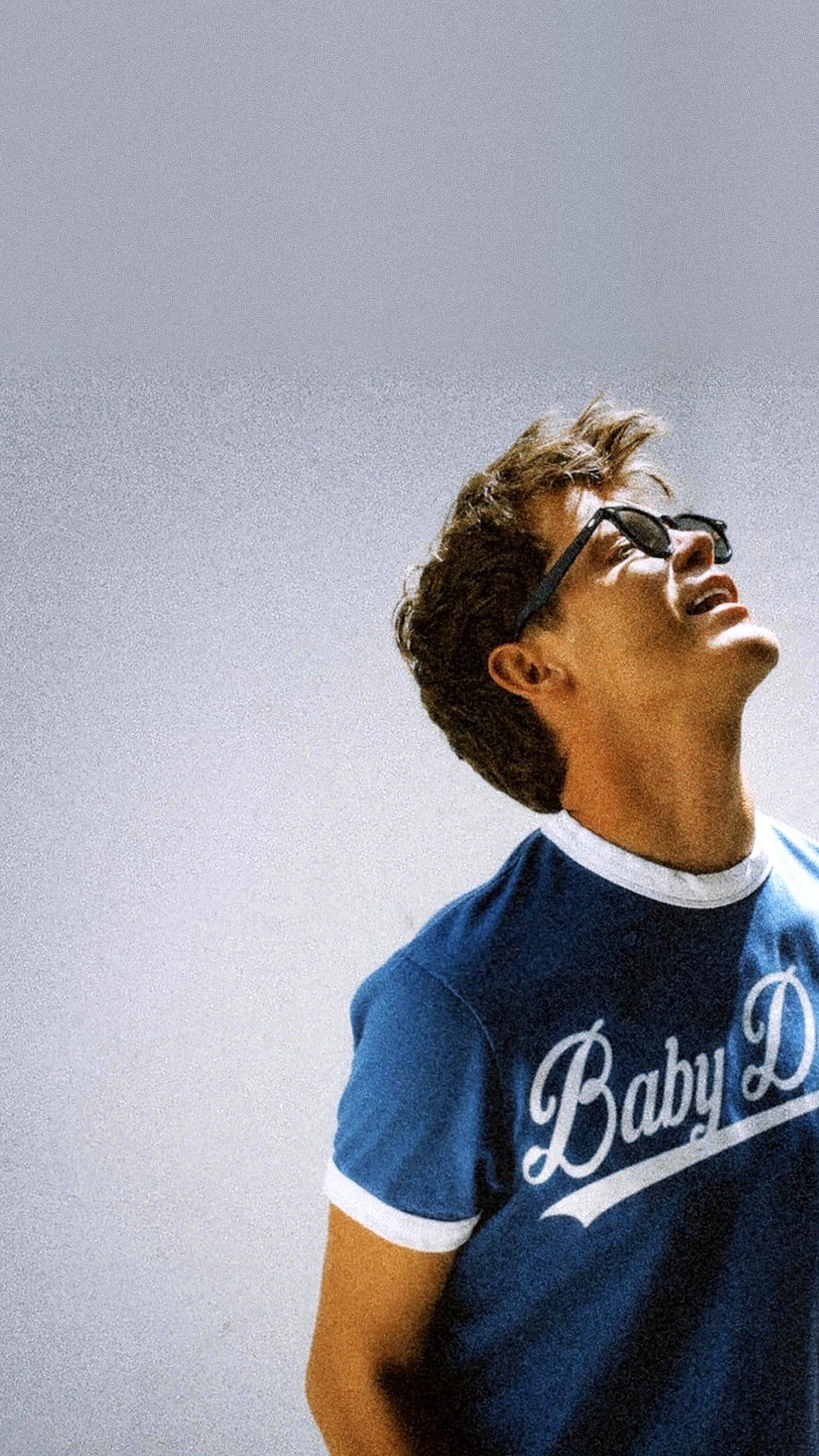 Jamie Miller in dark sunglasses tips his head back and smiles at the sky, wearing a blue ringer T-shirt with 'Baby Doll' written across it in white script, on the 'Babydoll' single artwork