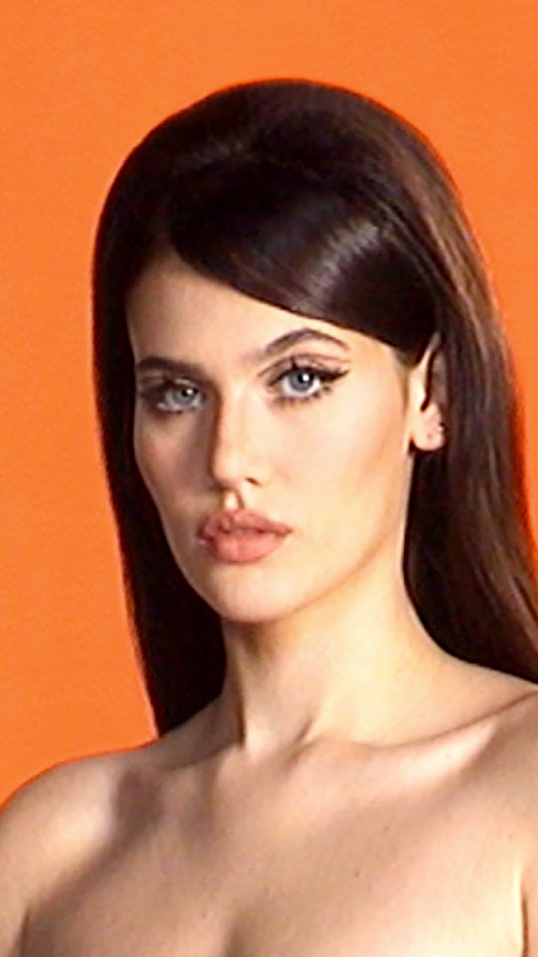 Sienna Spiro, her long dark hair swept to one side and her eyes lined in black, looks into the camera against an orange backdrop on the cover of her album 'Visitor'
