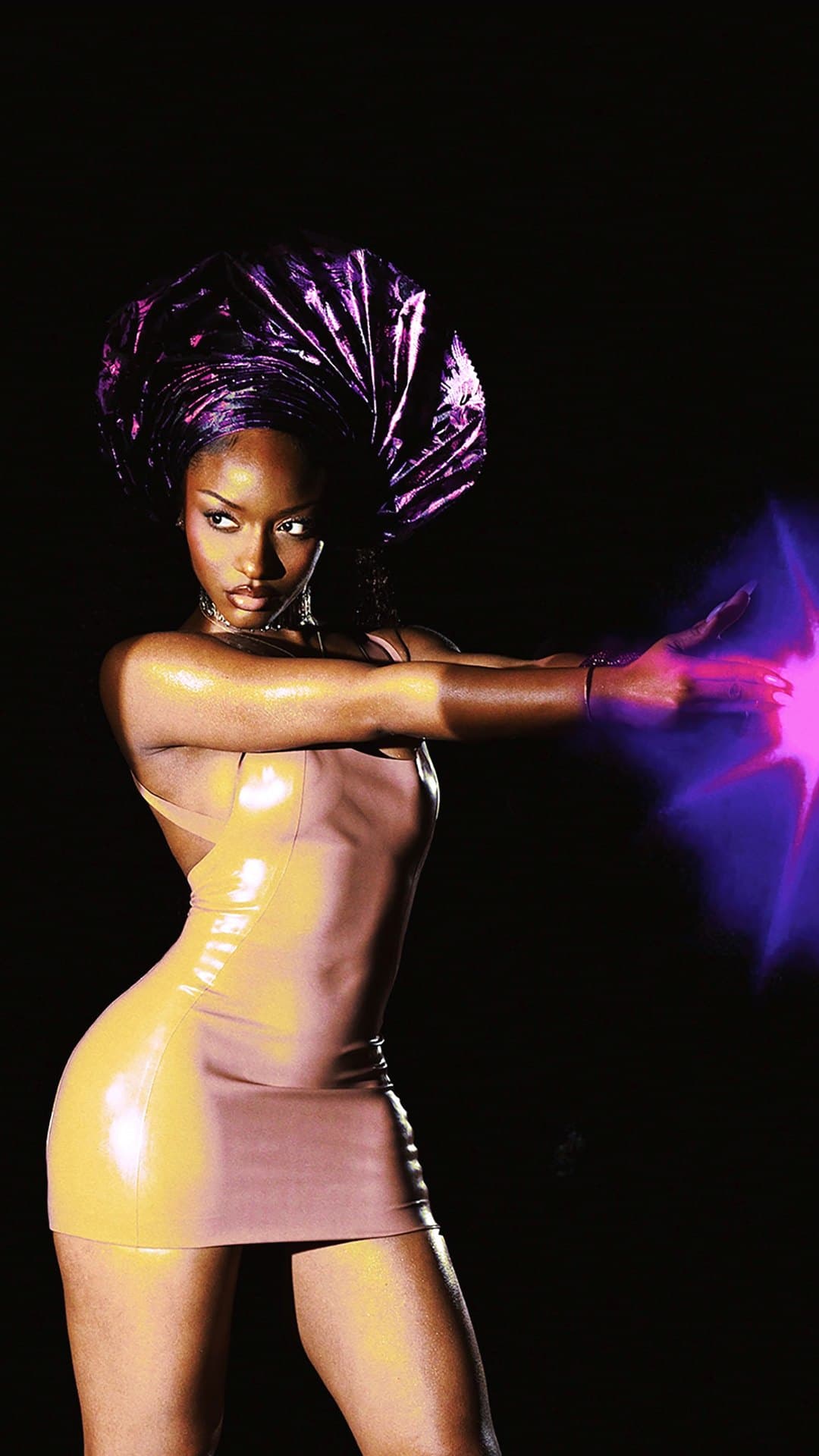Ayra Starr in a glossy gold mini dress and a purple metallic gele fires a pink beam of light from her outstretched hand against black, on the cover of her album 'Starrgirl'