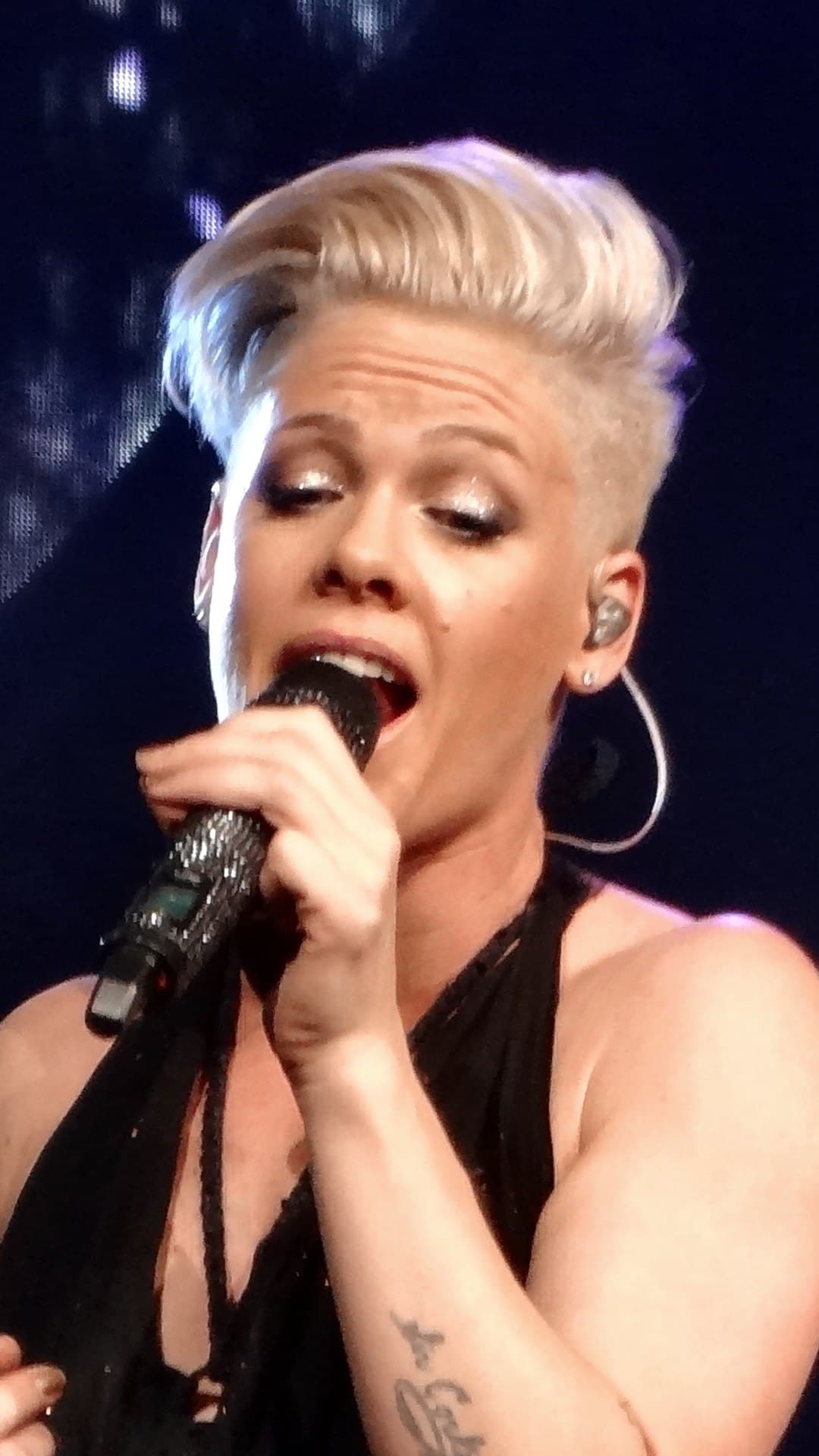 P!nk, her platinum hair swept up, sings into a microphone in a black halter dress on The Truth About Love Tour in March 2013