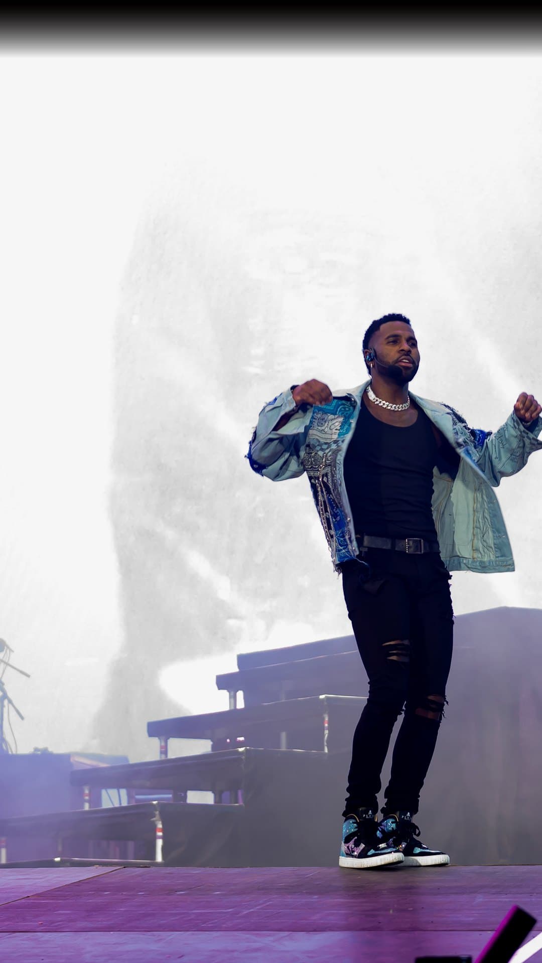 Jason Derulo, in an open patchwork denim jacket, a black vest, a chain and ripped black jeans, dances on stage against a white haze at the Superbloom festival in Munich in September 2023