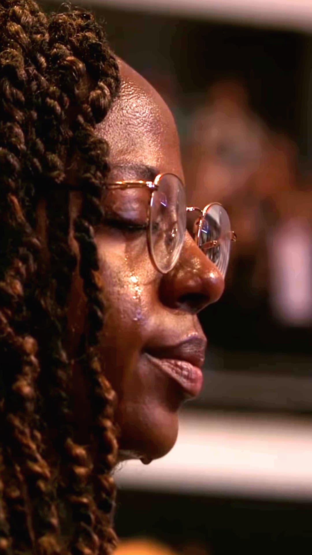 A woman with long braids and round glasses prays with her eyes closed, a tear on her cheek, a worshipper in the official visualizer for Sunvera Scott's 'Pray for Me'