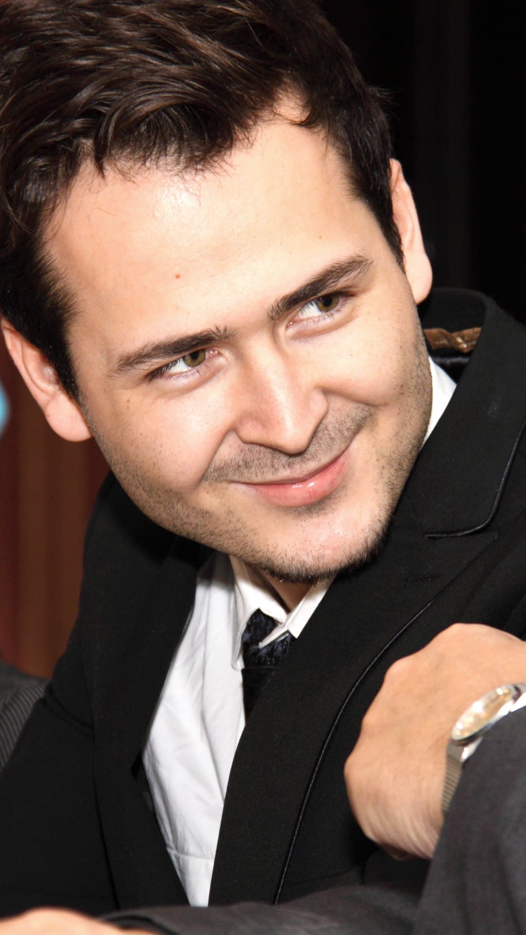 Edward Maya, producer of 'Stereo Love', smiles over his shoulder in a dark suit, white shirt and tie in front of a red curtain, at a meeting in January 2010