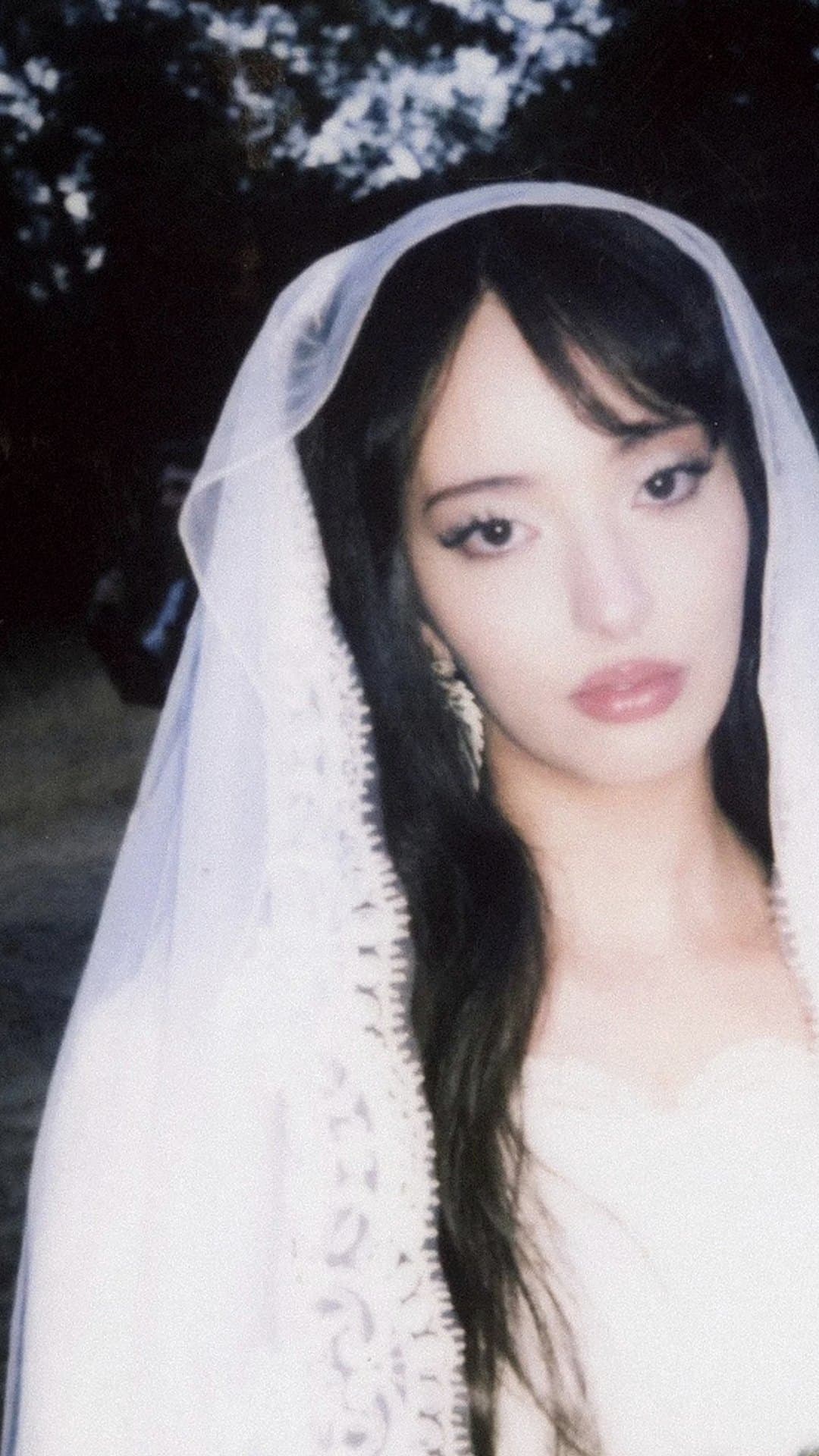 Faouzia, in a sheer white lace-edged veil over long dark hair, with dark eyeliner and pink lips, looks into the camera in a wooded clearing at dusk, on the cover of her single 'UNETHICAL'