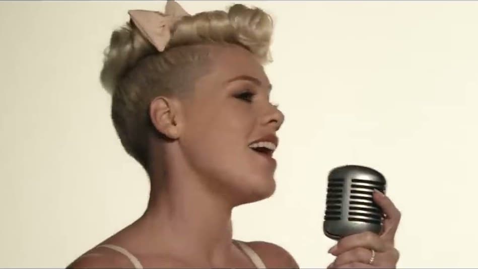 P!nk, a pale bow in her short blonde hair, sings into a vintage silver microphone against a white wall in the 'Just Give Me a Reason' video