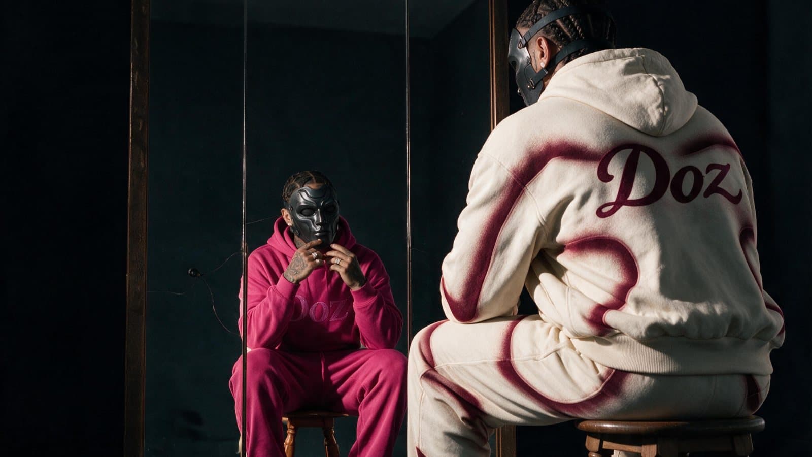 Doz, seen from behind in a cream hooded tracksuit with 'Doz' on the back, sits on a wooden stool facing a mirror in which a masked figure in a pink tracksuit looks out at the camera, on the cover of the EP DEUXIÈME DOSE